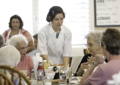 A woman serving food to elderly people at a table during a dining event.