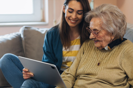 A woman and an older woman sitting on a couch, with the younger woman wearing a One Size Fits all Jumper, using a tablet.