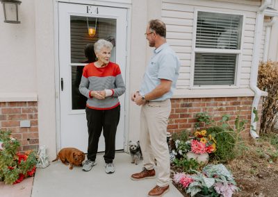A man and woman talking with their dog posing in front of a house, showcasing the beautiful outdoor spaces.