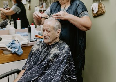 Female hairdresser trimming an elderly man's hair in a salon.