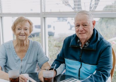 An elderly couple enjoying drinks and food at a table, sharing a moment together.